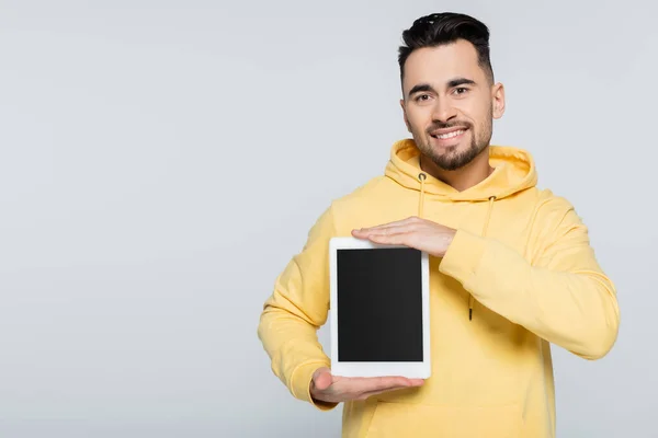 Hombre feliz con capucha amarilla sosteniendo tableta digital con pantalla en blanco aislada en gris - foto de stock