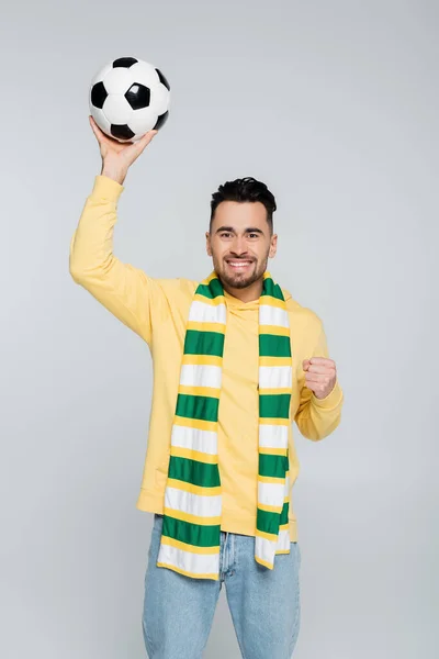 Appassionato di sport eccitato tenendo palla da calcio e mostrando vincere gesto isolato su grigio — Foto stock