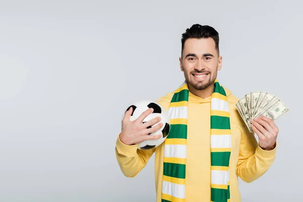Щасливий букмекер з футбольним м'ячем і доларовими банкнотами, дивлячись на камеру ізольовано на сірому — стокове фото