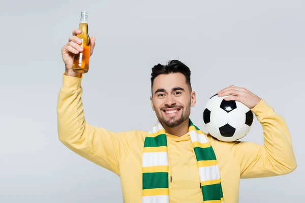 Joyful sports fan with soccer ball and bottle of beer smiling at camera isolated on grey — Photo de stock