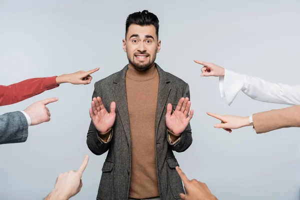 Shocked critic showing stop gesture near people pointing with fingers isolated on grey — Stock Photo