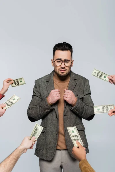 Embarrassed critic in eyeglasses near people with dollar banknotes isolated on grey — стоковое фото