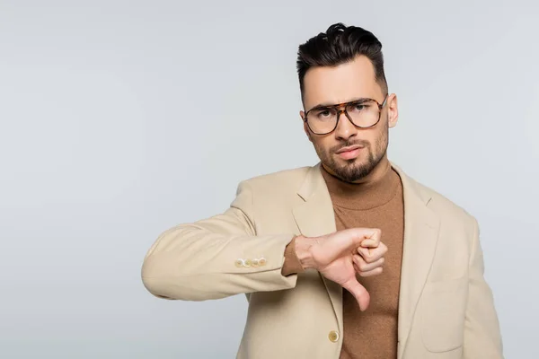 Crítico disgustado en gafas que muestran el pulgar hacia abajo mientras mira la cámara aislada en gris - foto de stock