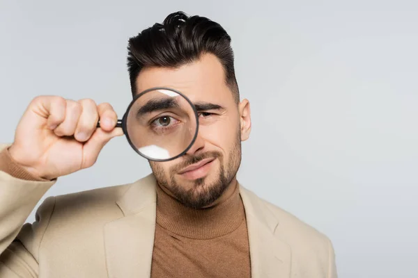 Picky critic looking at camera through magnifying glass isolated on grey — Foto stock