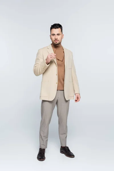 Full length of critic in beige blazer and trousers holding eyeglasses on grey — Photo de stock