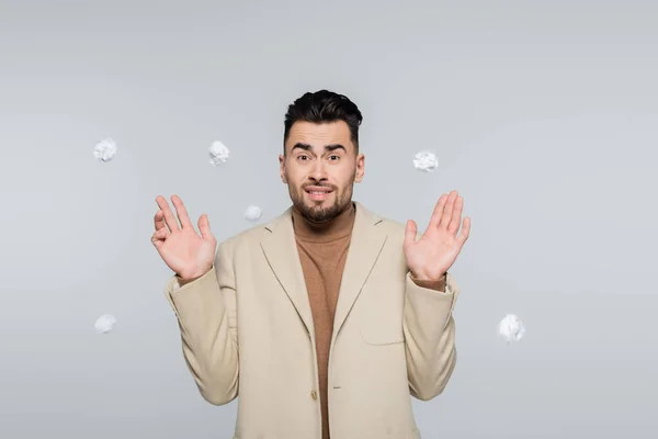 Frightened critic gesturing near flying crumpled paper isolated on grey - foto de stock