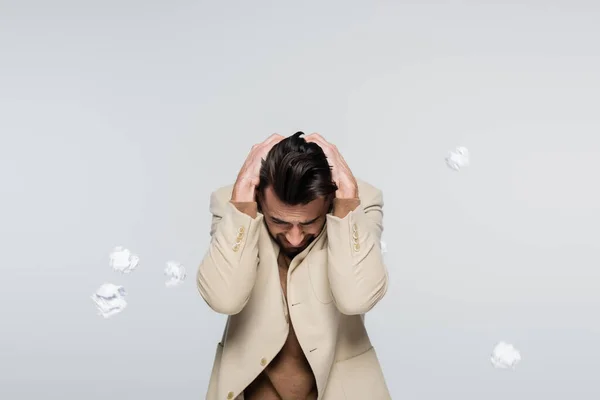 Frightened critic covering head with hands near flying crumpled paper isolated on grey - foto de stock