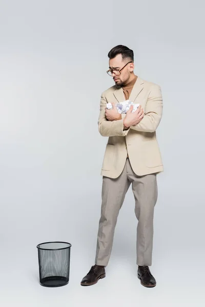 Full length view of critic with crumpled paper standing near trash can on grey — Stockfoto