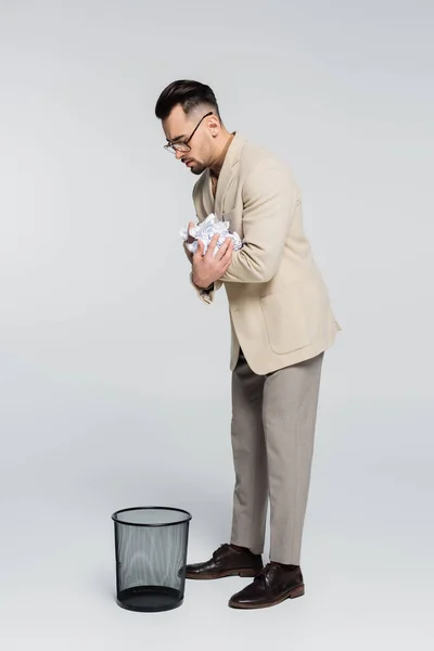 Visão de comprimento total do crítico segurando papel amassado perto da lata de lixo em cinza — Fotografia de Stock