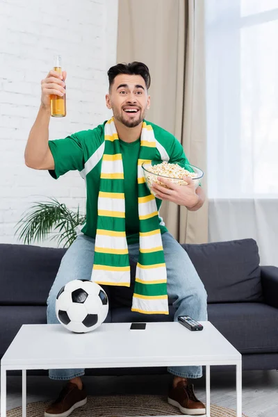 Fan de sport joyeux avec bière et championnat d'observation de maïs soufflé près du ballon de football — Photo de stock