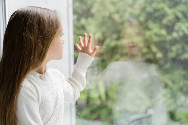 Menina com cabelo longo tocando vidro da janela com gotas de chuva — Fotografia de Stock