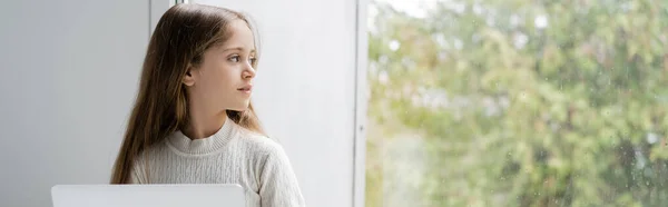 Fille avec ordinateur portable regardant par la fenêtre à la maison, bannière — Photo de stock