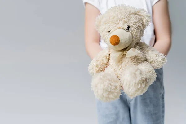 Vista parcial de chica borrosa sosteniendo osito de peluche aislado en gris - foto de stock