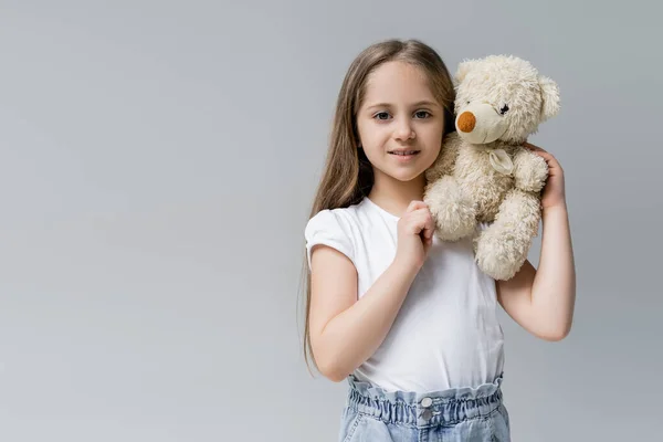 Lächelndes Mädchen mit Teddybär, das isoliert auf grau in die Kamera blickt — Stockfoto