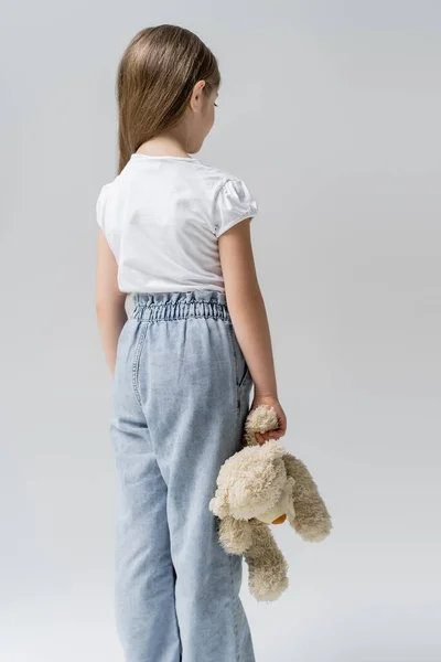 Back view of frustrated girl standing with teddy bear isolated on grey — Stock Photo