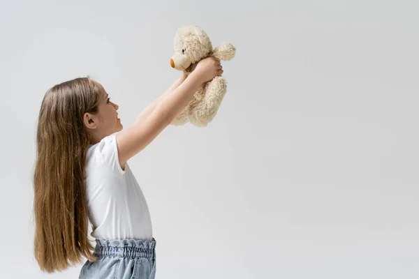 Vista laterale della ragazza con i capelli lunghi tenendo orsacchiotto isolato su grigio — Foto stock