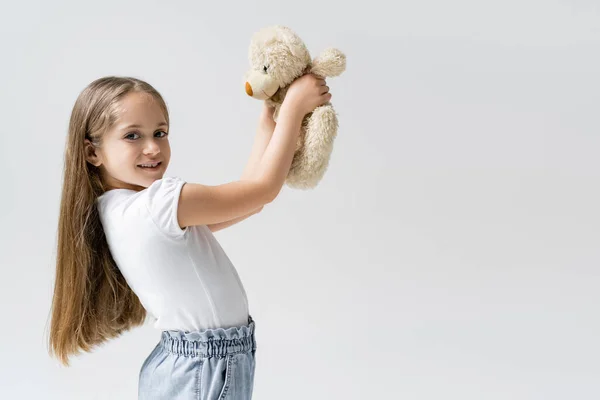 Happy girl with teddy bear smiling at camera isolated on grey — Stock Photo