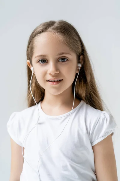 Joyful girl in earphones and white t-shirt looking at camera isolated on grey — Stock Photo