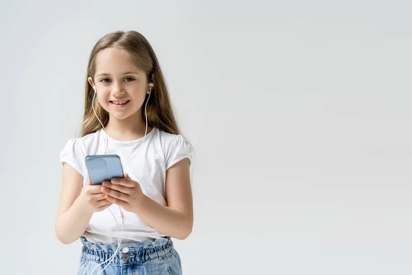 Bambino felice con auricolari e cellulare guardando la fotocamera isolata su grigio — Foto stock