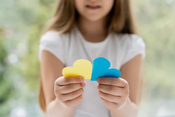 Vista parcial de chica borrosa sosteniendo corazones de papel azul y amarillo - foto de stock