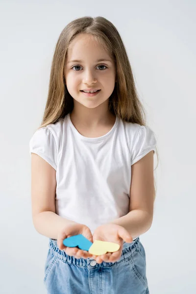 Smiling girl with long hair and blue and yellow paper hearts isolated on grey — Stock Photo