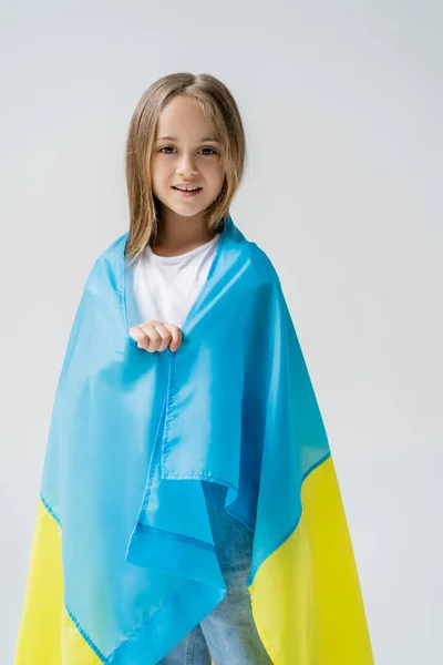 Патриотичная девушка, покрытая украинским флагом, улыбающаяся в камеру, изолированную на сером — стоковое фото