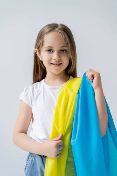 Smiling kid looking at camera and holding ukrainian flag isolated on grey — Stock Photo