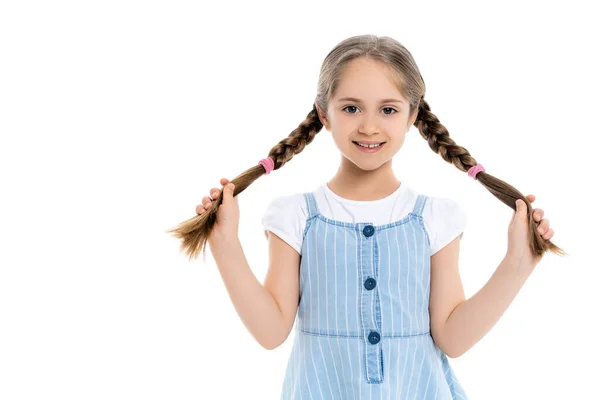 Fille gaie en robe à sangle bleue tenant des tresses isolées sur blanc — Photo de stock