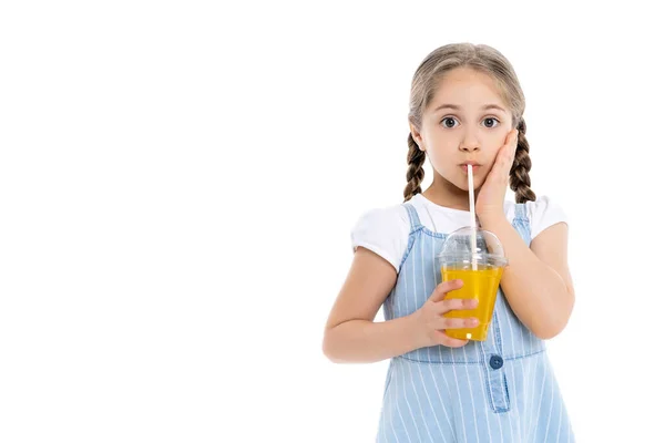 Stupito ragazza toccare il viso mentre beve succo d'arancia isolato su bianco — Foto stock