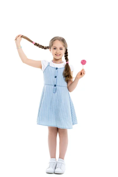 Full length view of cheerful girl holding braid and lollipop on white — Stock Photo