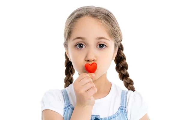 Girl with braids kissing red toy heart and looking at camera isolated on white — Stock Photo