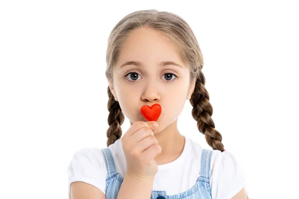 Chica con trenzas besar rojo juguete corazón y mirando cámara aislada en blanco - foto de stock