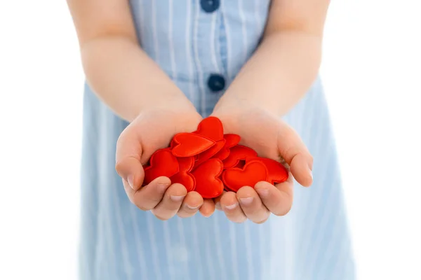 Abgeschnittene Ansicht eines verschwommenen Mädchens mit einer Handvoll roter Spielzeugherzen auf weißem Grund — Stockfoto