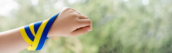 Cropped view of patriotic child with blue and yellow ribbon on hand, banner — Stock Photo