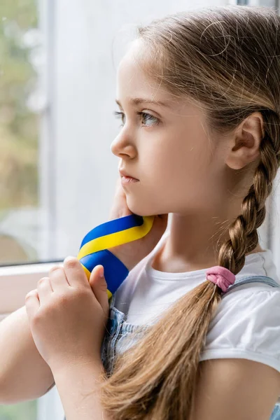 Вдумлива українська дівчина з синьо-жовтою стрічкою дивиться вдома — Stock Photo