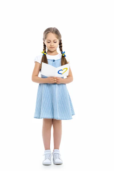 Повний вигляд дівчини, що читає листівку з синьо-жовтим серцем на білому — стокове фото