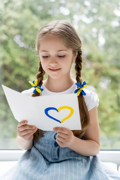 Positive patriotic girl reading postcard with blue and yellow heart — Stock Photo