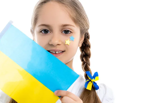 Chica patriótica con estrellas azules y amarillas de la cara sosteniendo pequeña bandera ucraniana aislada en blanco — Stock Photo