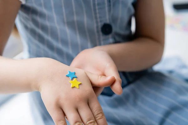 Cropped view of child with blue and yellow stars on hand — Stock Photo