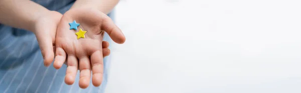 Partial view of blurred girl holding blue and yellow stars on grey background, banner — Stock Photo