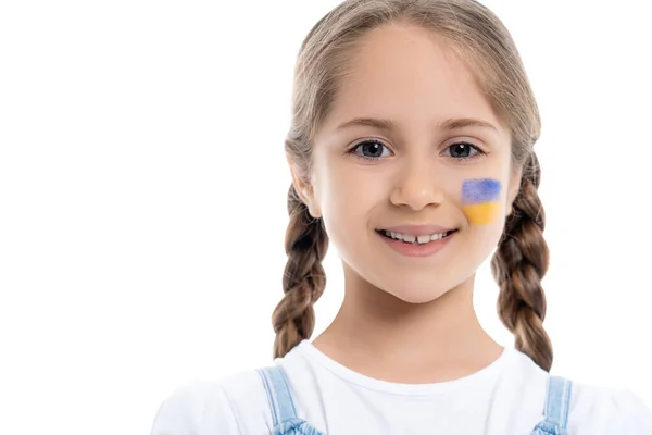 Щаслива дівчина з косами та українським прапором на щоці дивиться на камеру ізольовано на білому — стокове фото
