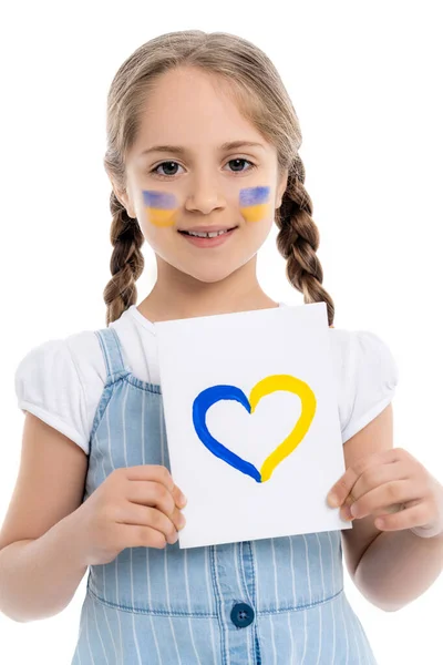 Girl with ukrainian flags on face holding card with blue and yellow heart isolated on white — Stock Photo