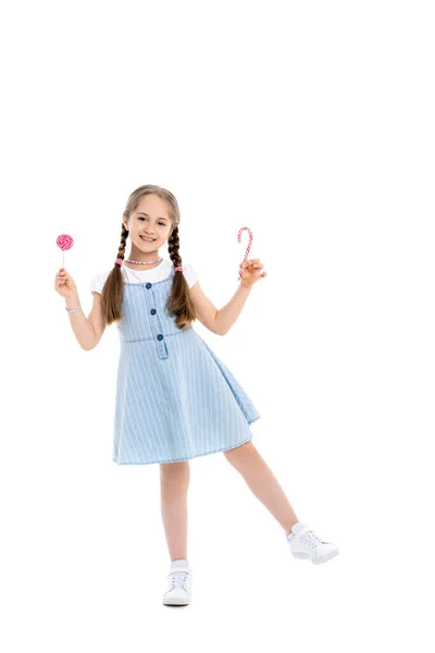 Full length view of cheerful girl with candy cane and lollipop on white — Stock Photo