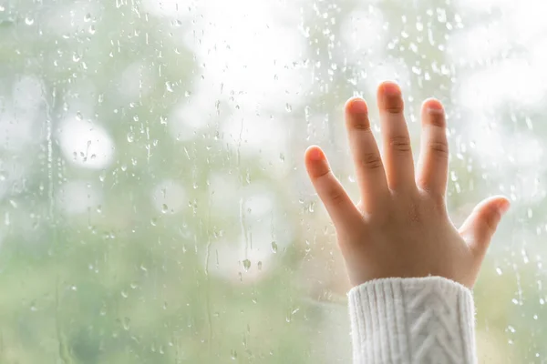 Partial view of kid touching window glass with raindrops — Stock Photo