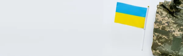 Верхний вид украинского флага возле военной формы на белом фоне, баннер — стоковое фото