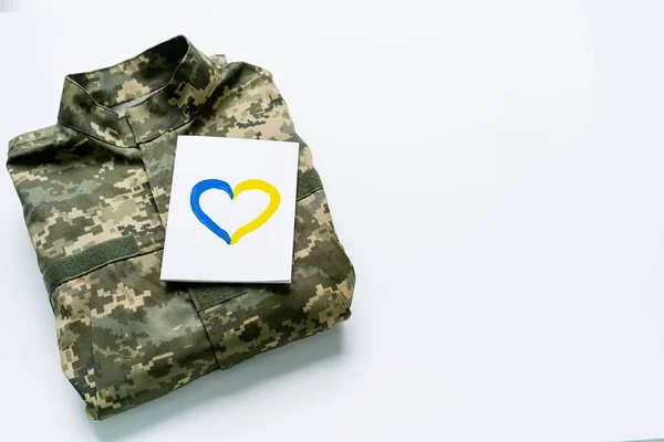 Top view of card with blue and yellow heart sign on military uniform on white background — Stock Photo