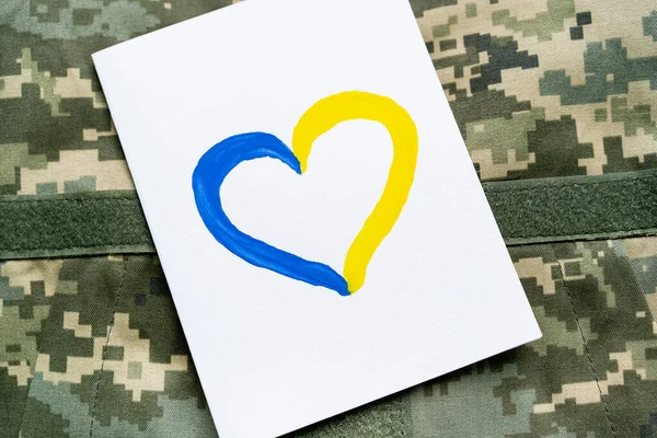 Vue du dessus de la carte avec le signe de coeur bleu et jaune sur l'uniforme militaire — Photo de stock