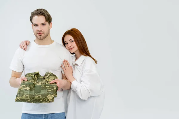 Young woman hugging boyfriend holding military uniform isolated on white — Stock Photo