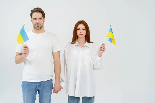 Jeune couple tenant la main et drapeaux ukrainiens isolés sur blanc — Photo de stock