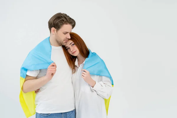 Young couple covered with ukrainian flag standing isolated on white — Stock Photo